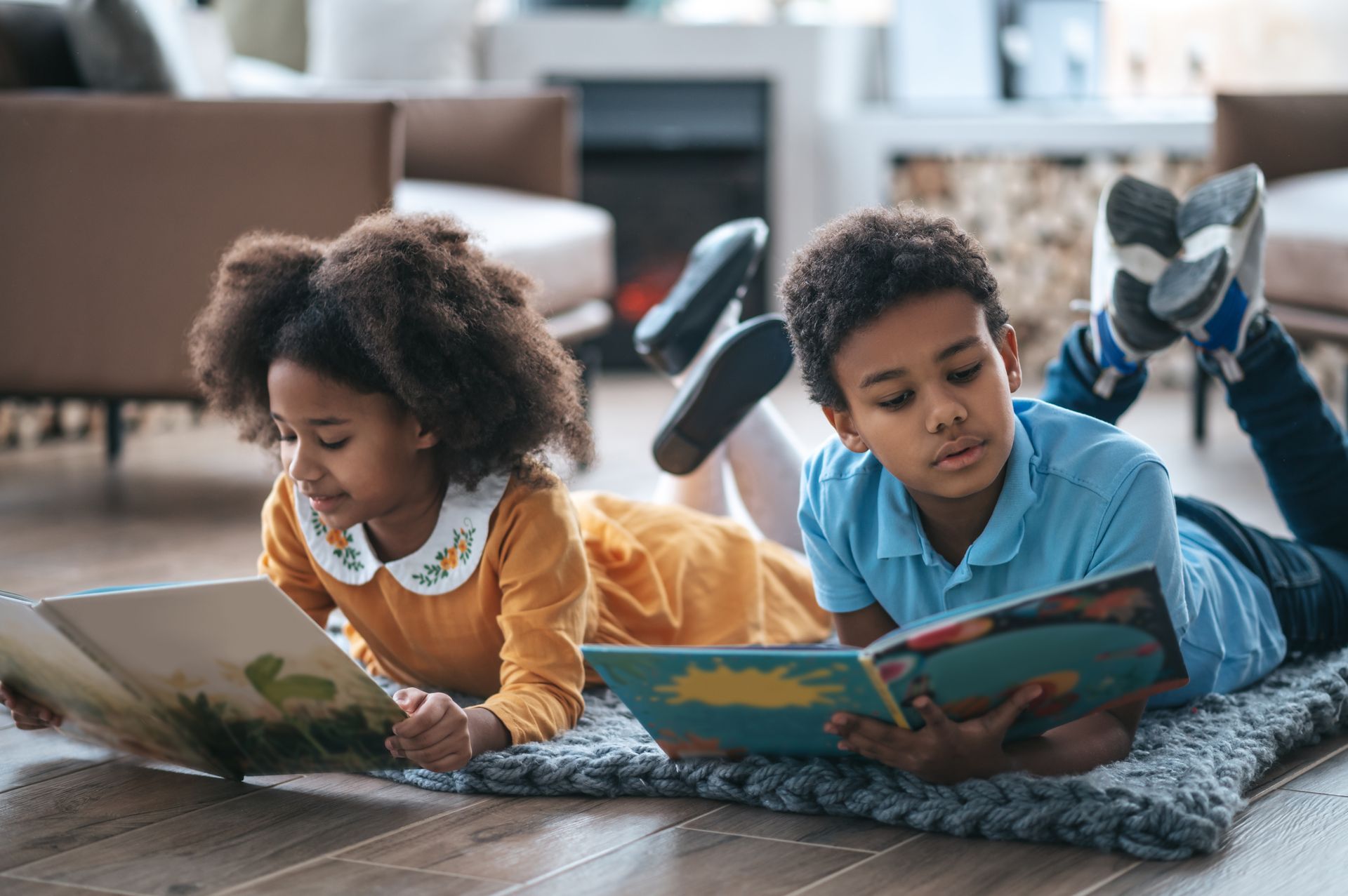 A boy and a girl are laying on the floor reading books.