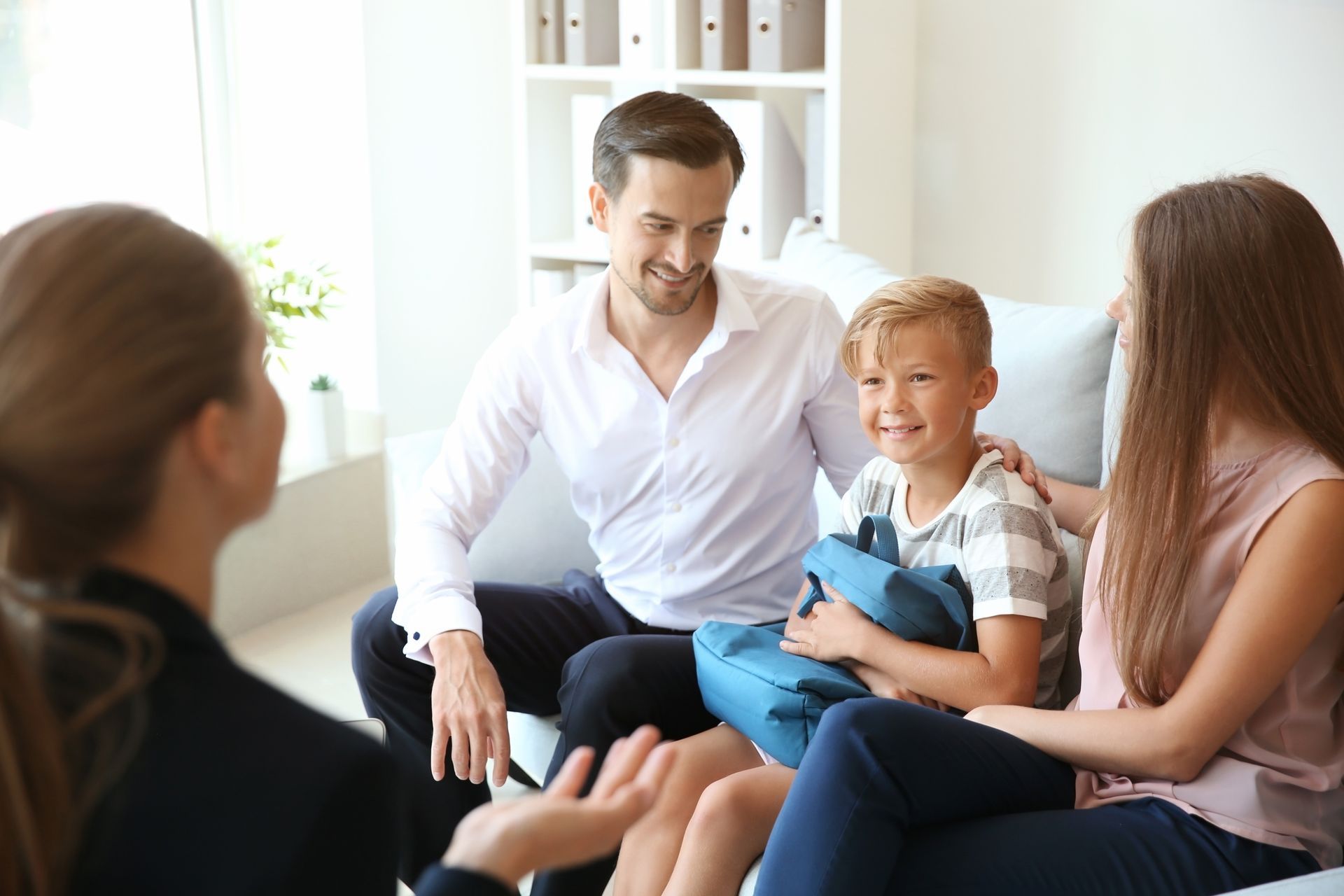 A family is sitting on a couch talking to a woman.