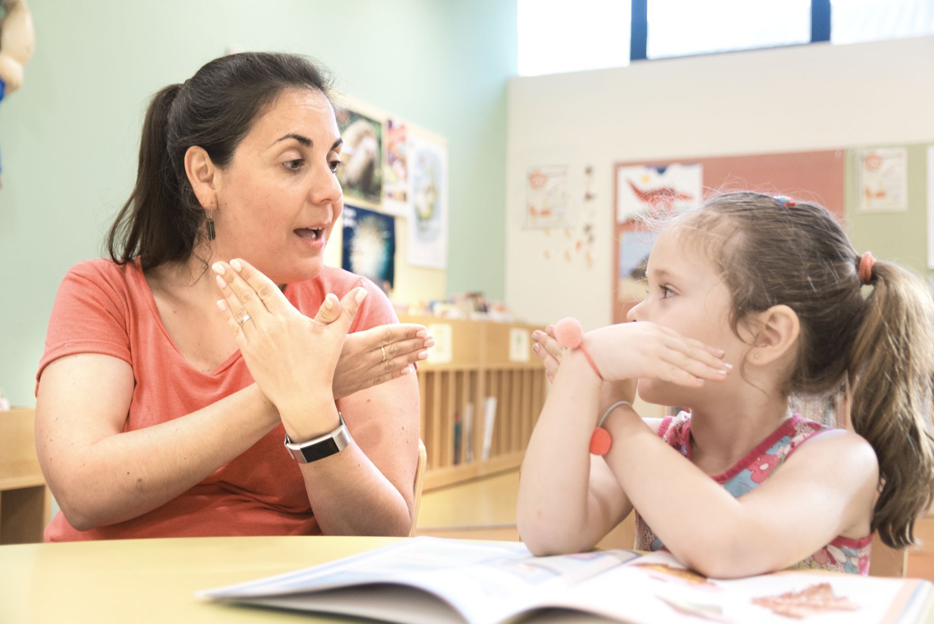 A woman and a little girl are sitting at a table talking to each other.