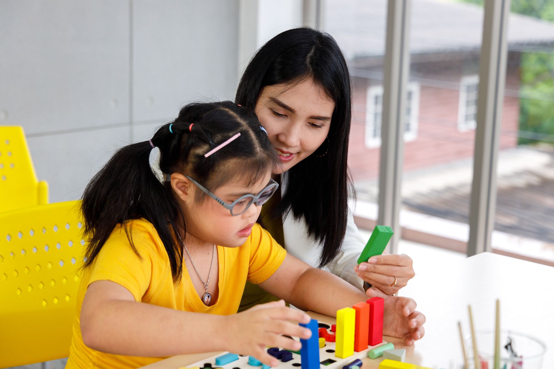 A woman is teaching a little girl how to play with wooden blocks.