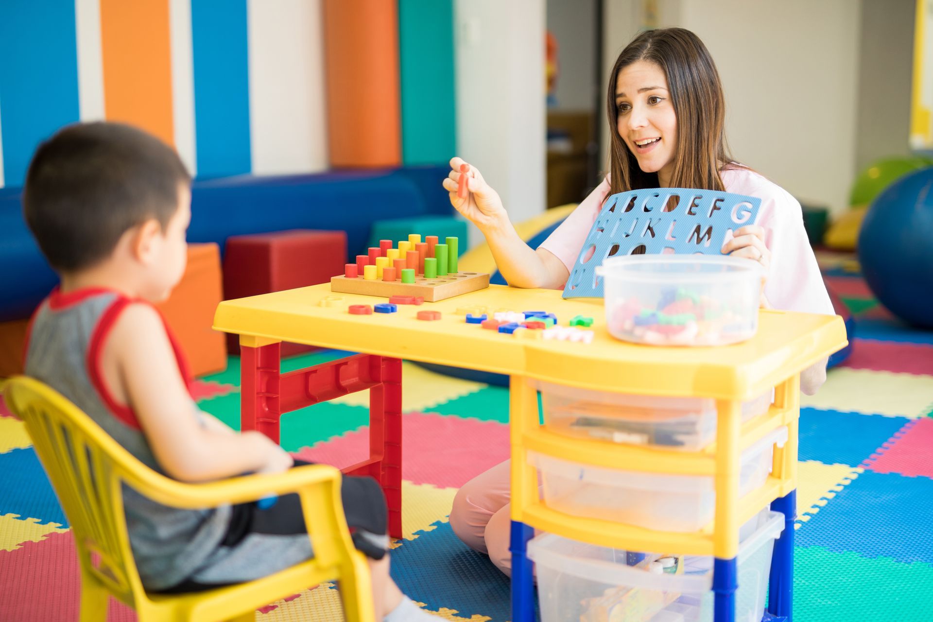 A woman is sitting at a table talking to a young boy.