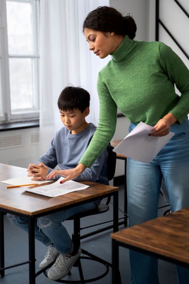 A woman is helping a young boy with his homework in a classroom.