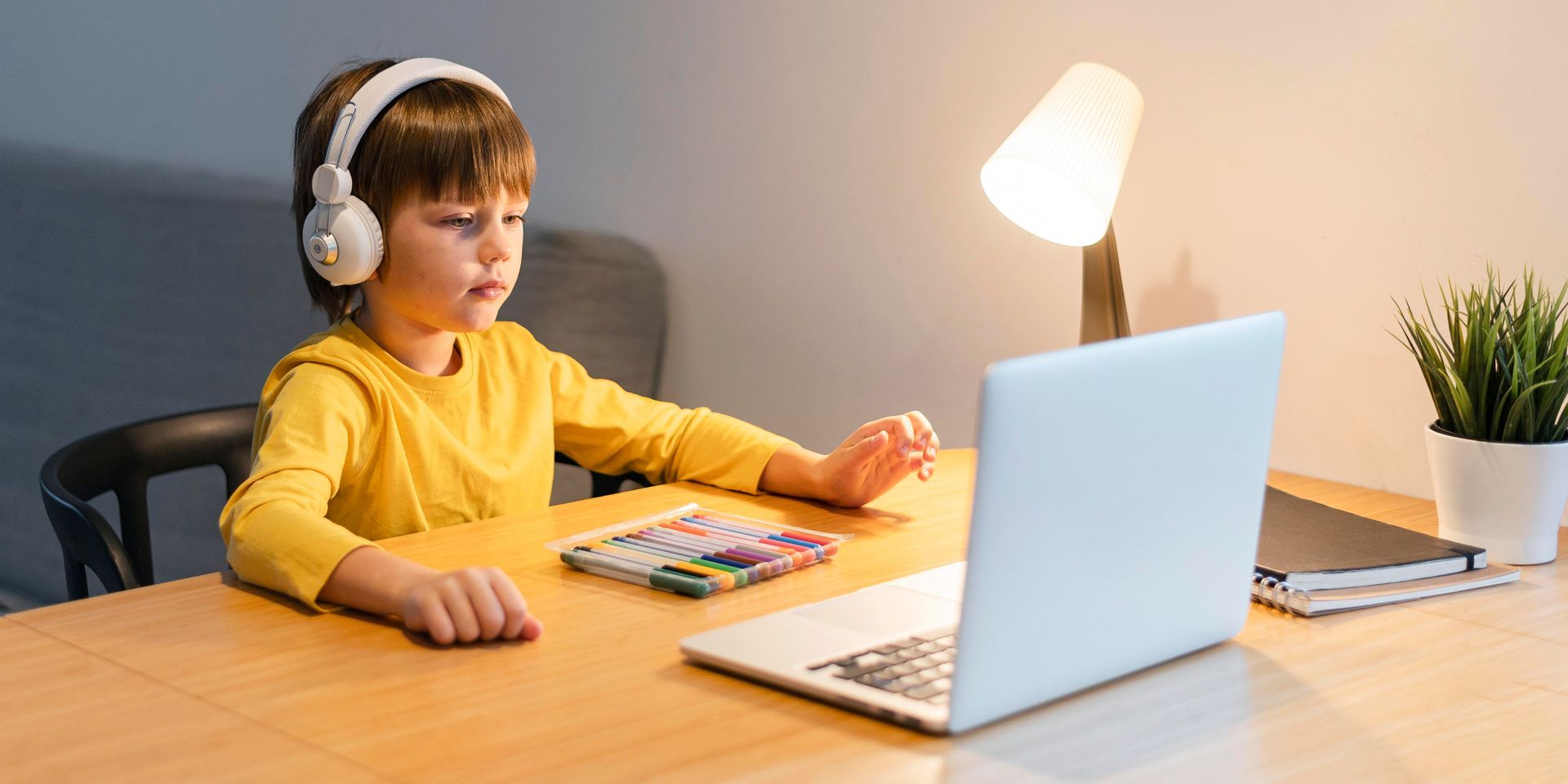A young boy wearing headphones is sitting at a table using a laptop computer.
