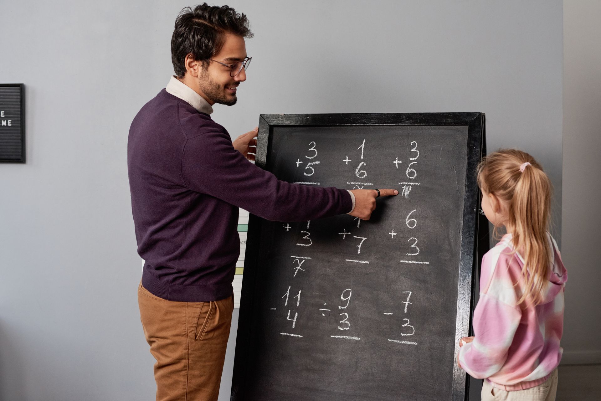 A man is pointing at a blackboard while a little girl looks on.