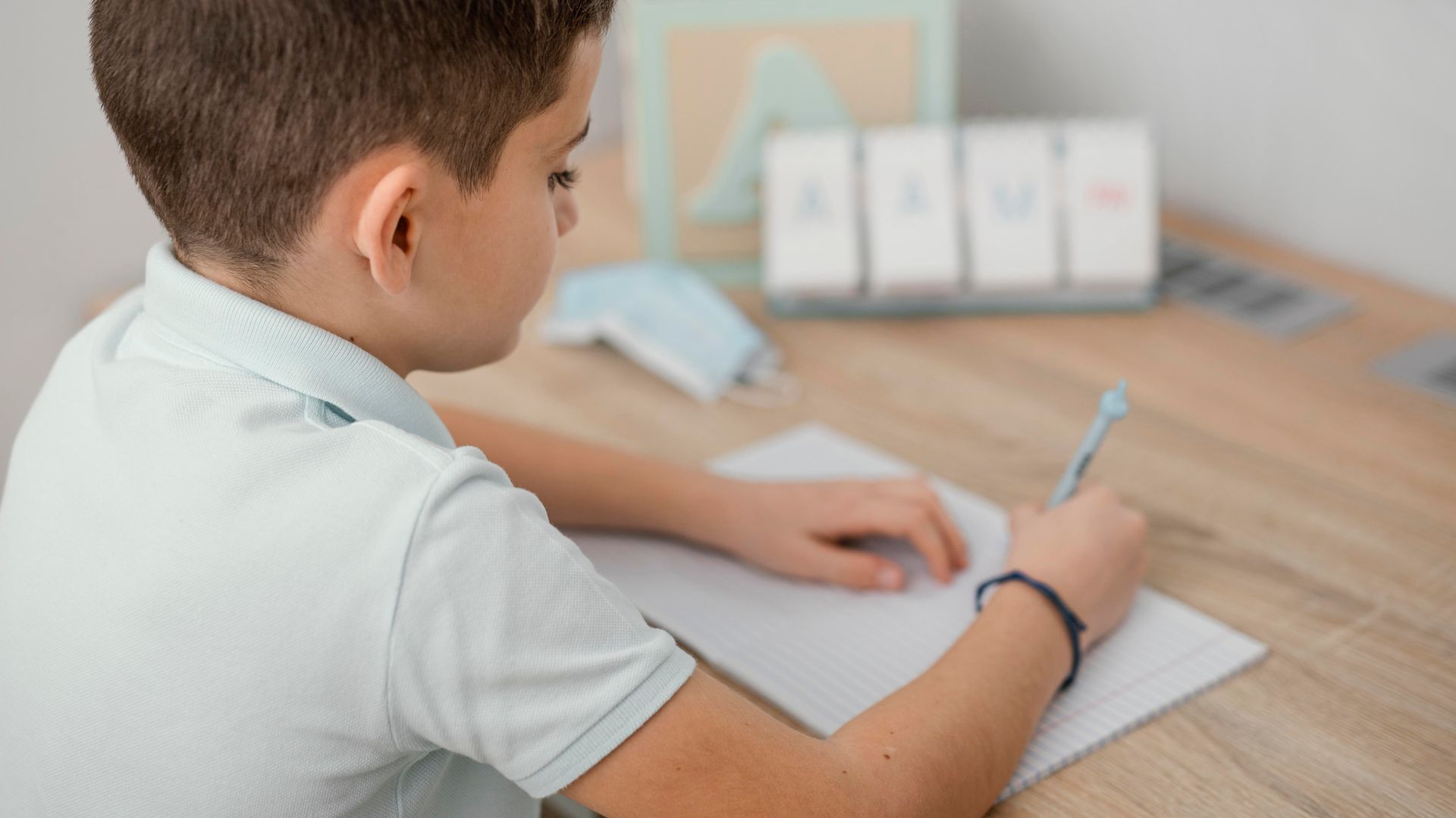 A young boy is sitting at a desk writing on a piece of paper.