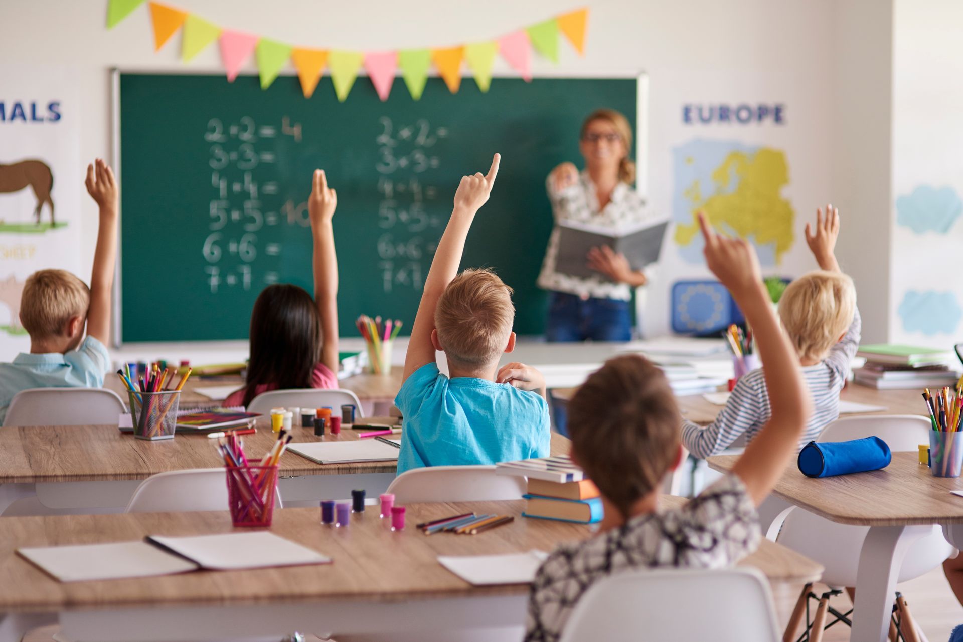 A group of children are raising their hands in a classroom to answer a question.