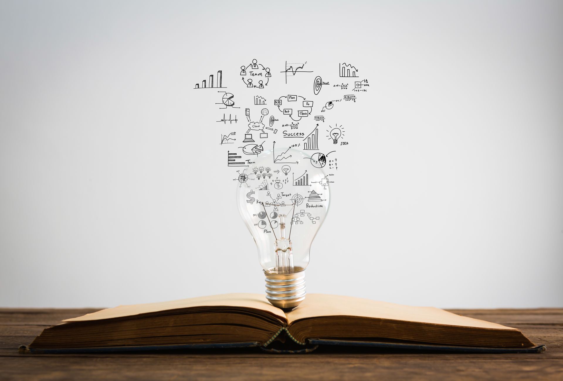 A light bulb is coming out of an open book on a wooden table.