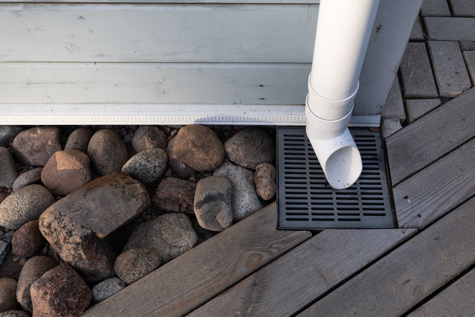 A white pipe is connected to a drain on a wooden deck.