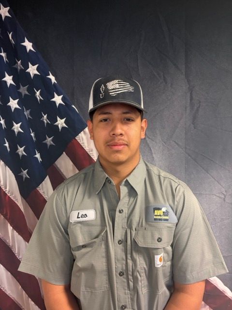 Man in work uniform with cap, standing in front of American flag.