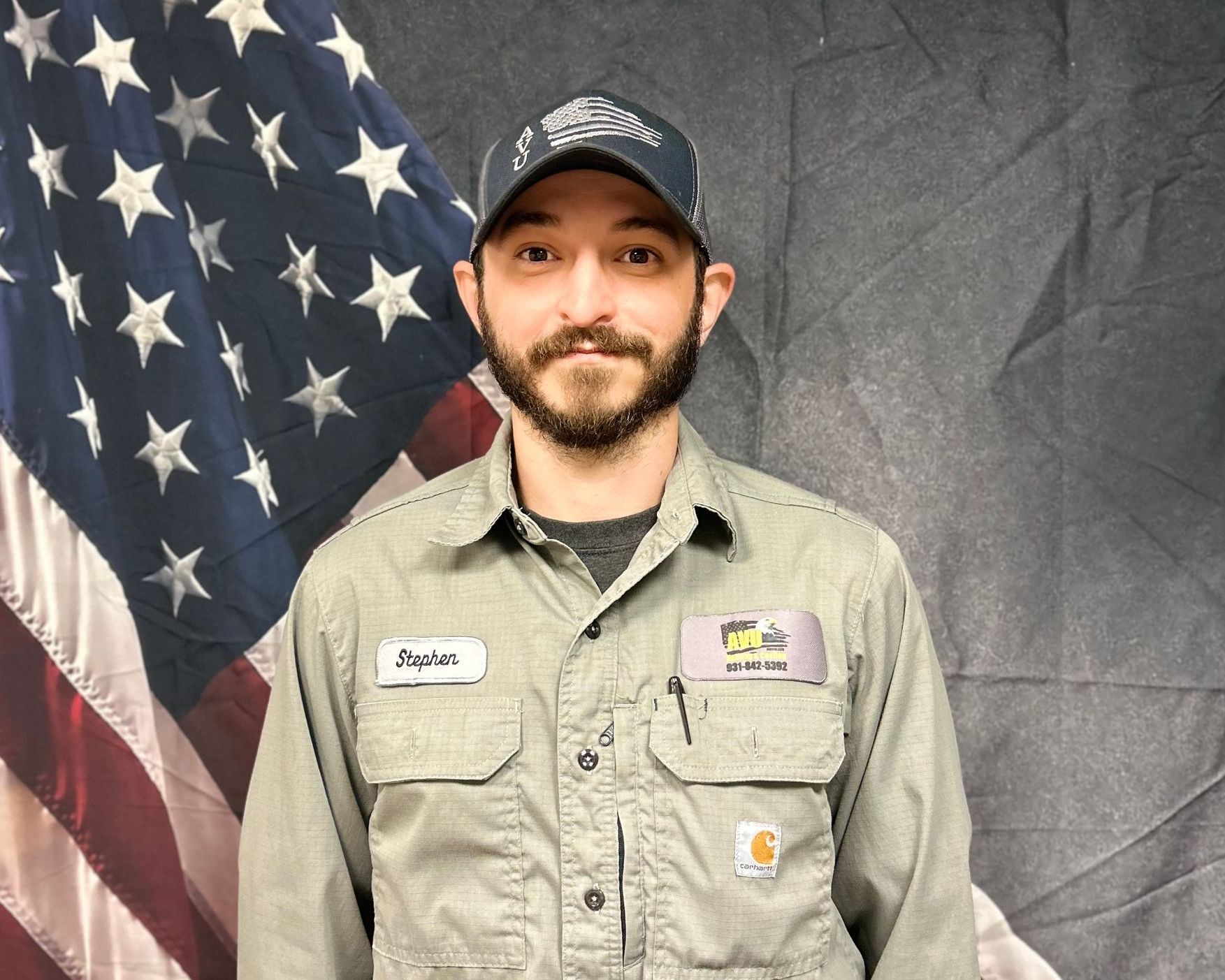 A man with a beard is standing in front of an american flag.
