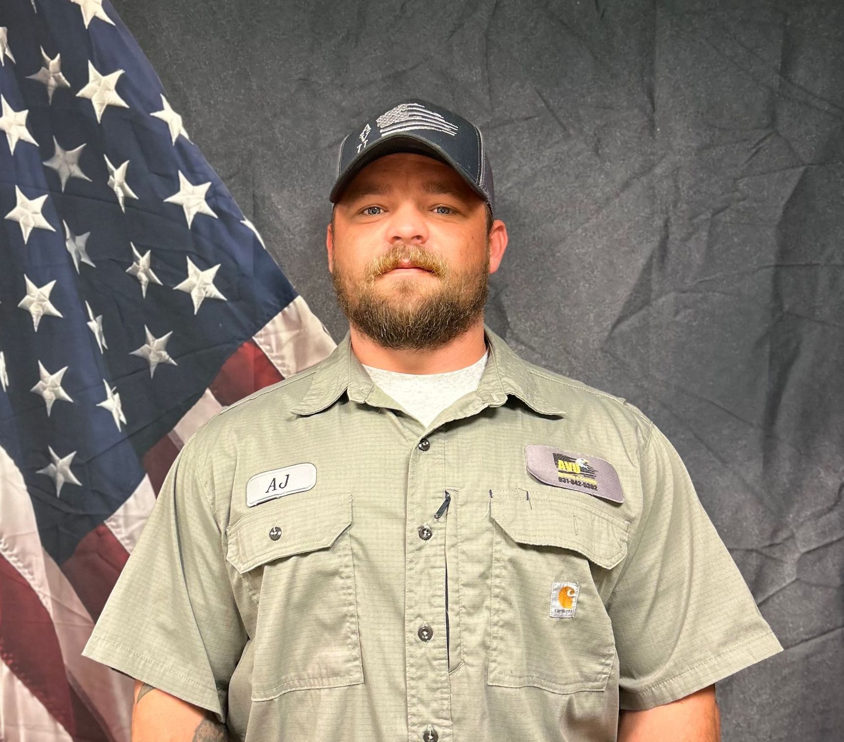 A man with a beard is standing in front of an american flag.