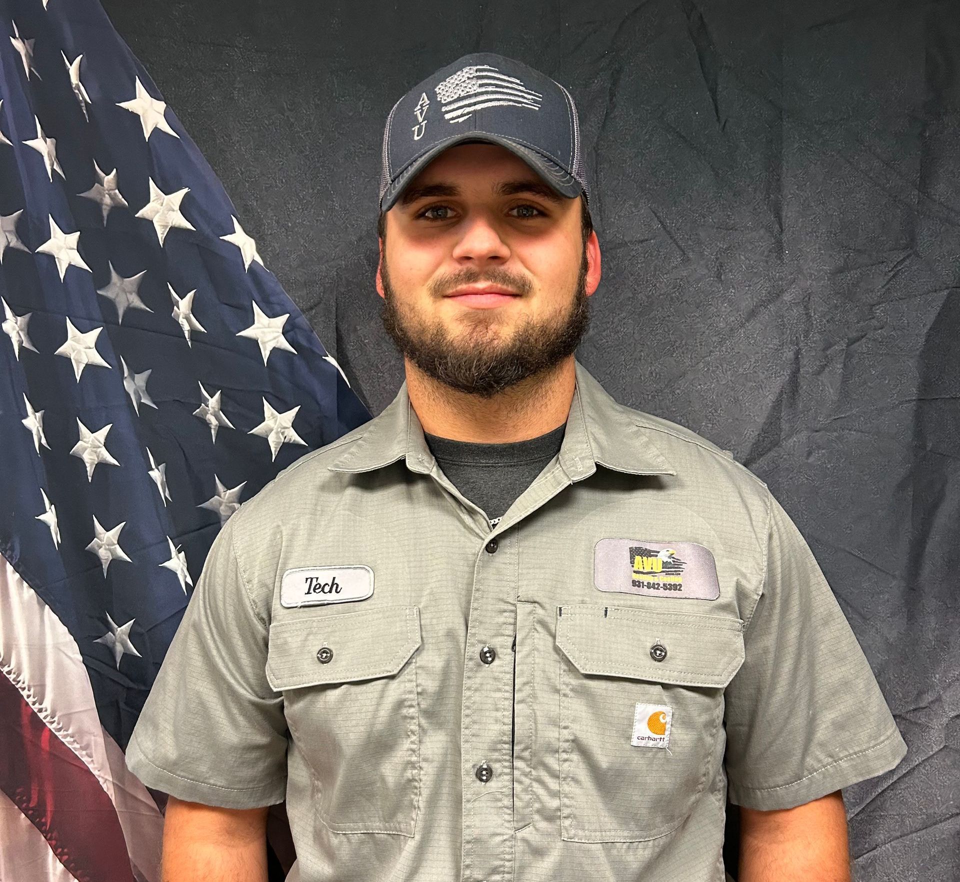 A man wearing a hat and a shirt is standing in front of an american flag.