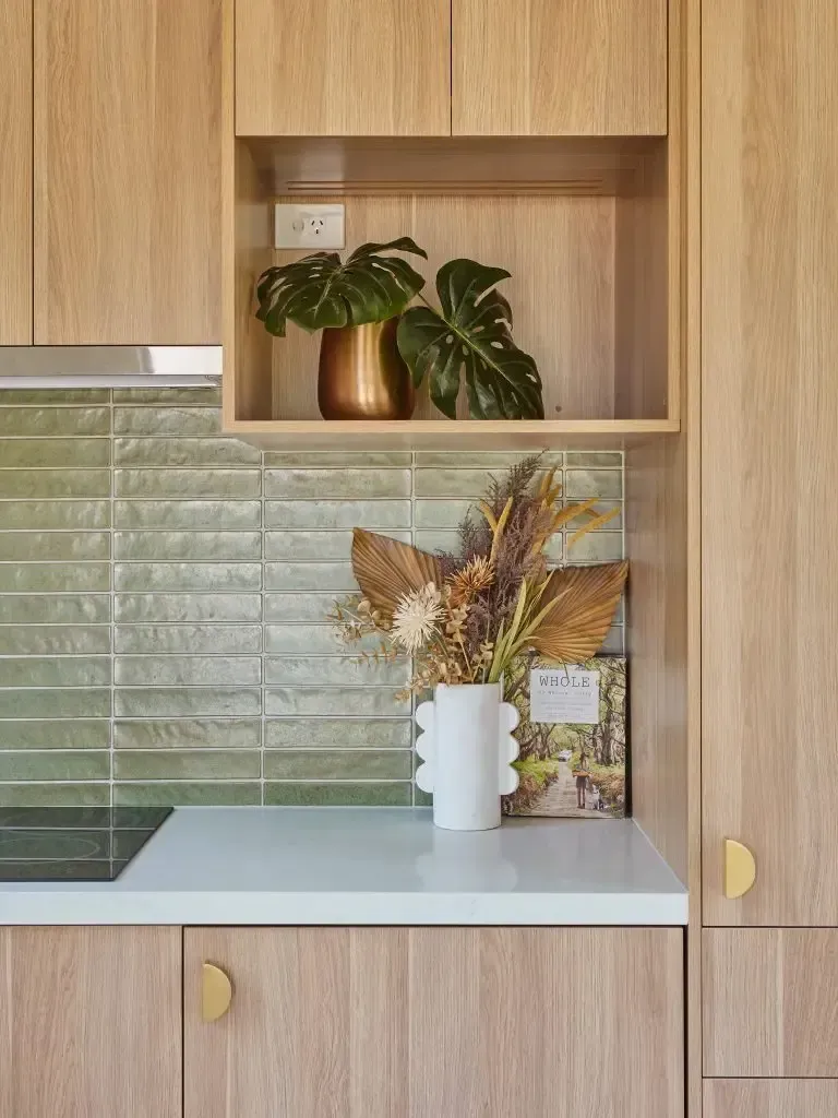 Kitchen with light wood cabinets, green backsplash, and decorations on the countertop and in a shelf.