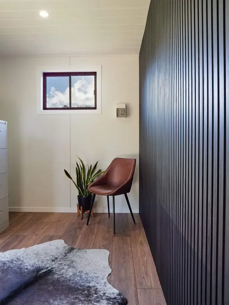 Room interior: chair, potted plant, cowhide rug, textured wall, window with cloudy sky.