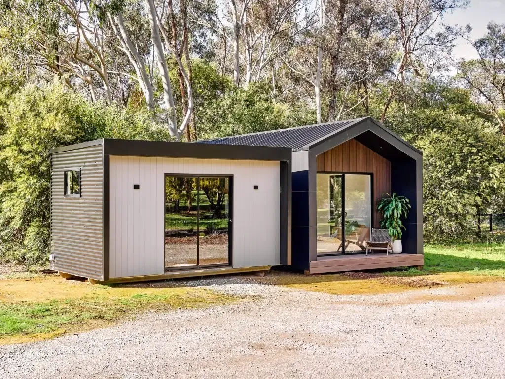 Modern cabin with two rectangular sections. One has sliding glass doors, the other, a small window. Set in grassy area with trees.