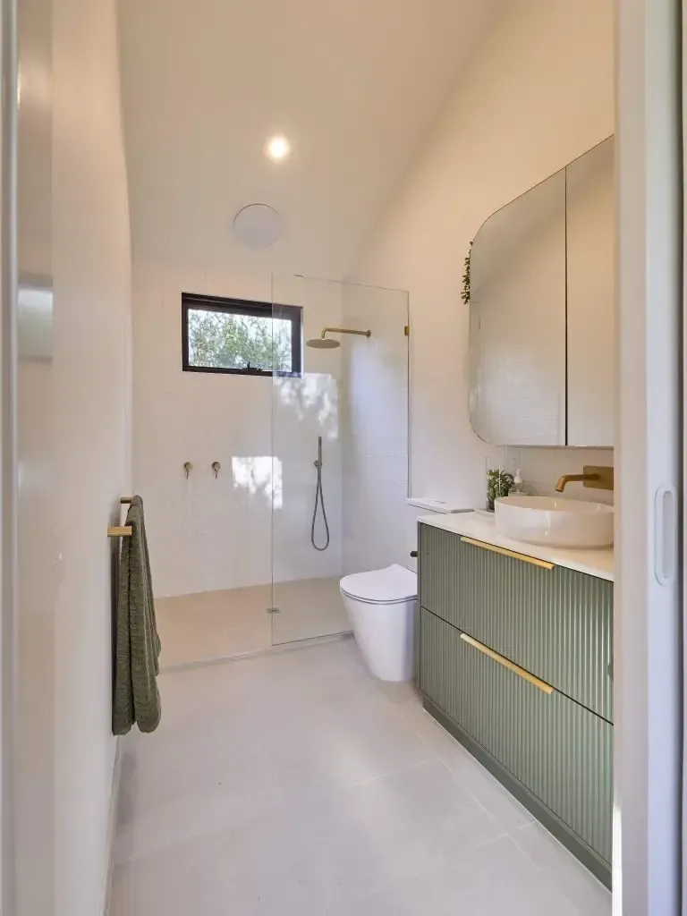 Bathroom with green vanity, gold fixtures, walk-in shower, and white walls.