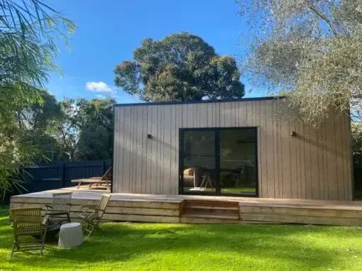 Wooden cabin with deck and sliding glass door, set in a grassy yard on a sunny day.