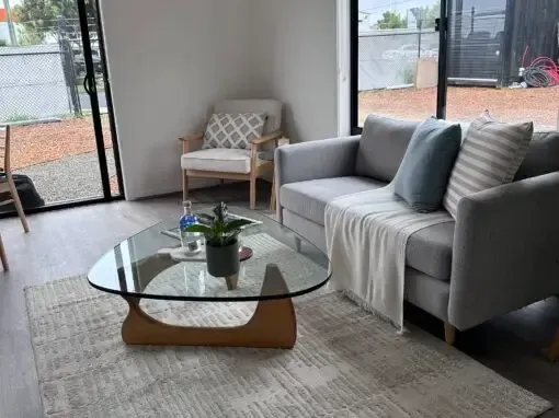 Living room with gray couch, wooden chair, glass coffee table, and rug.