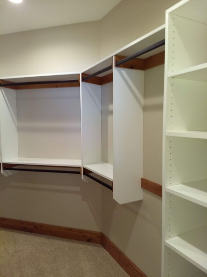 A walk in closet with white shelves and clothes racks