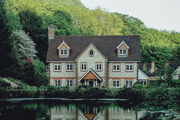 a large house is sitting on the shore of a lake surrounded by trees .