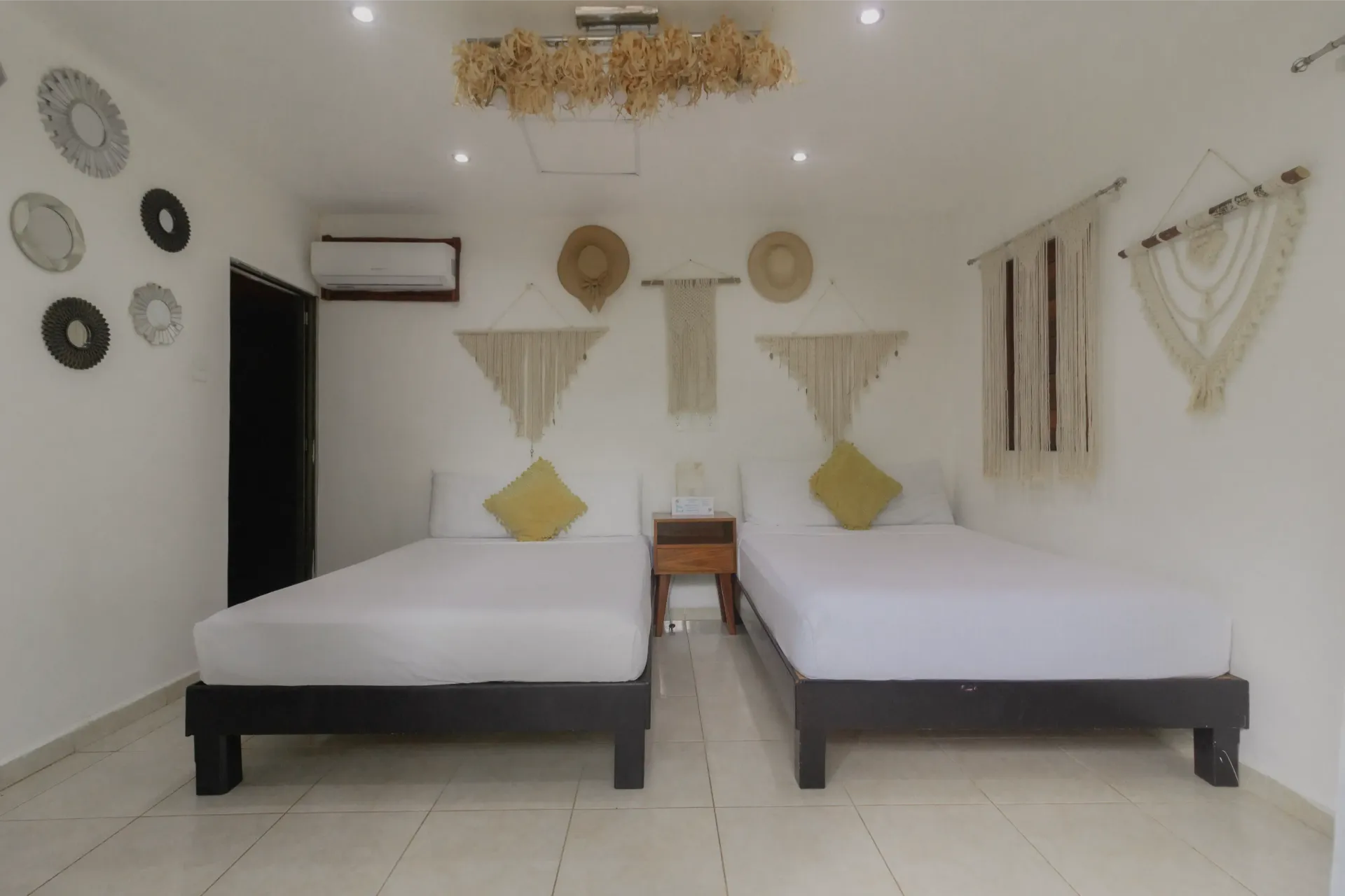 Habitación minimalista con dos camas individuales, paredes blancas, decoración mural y aire acondicionado.