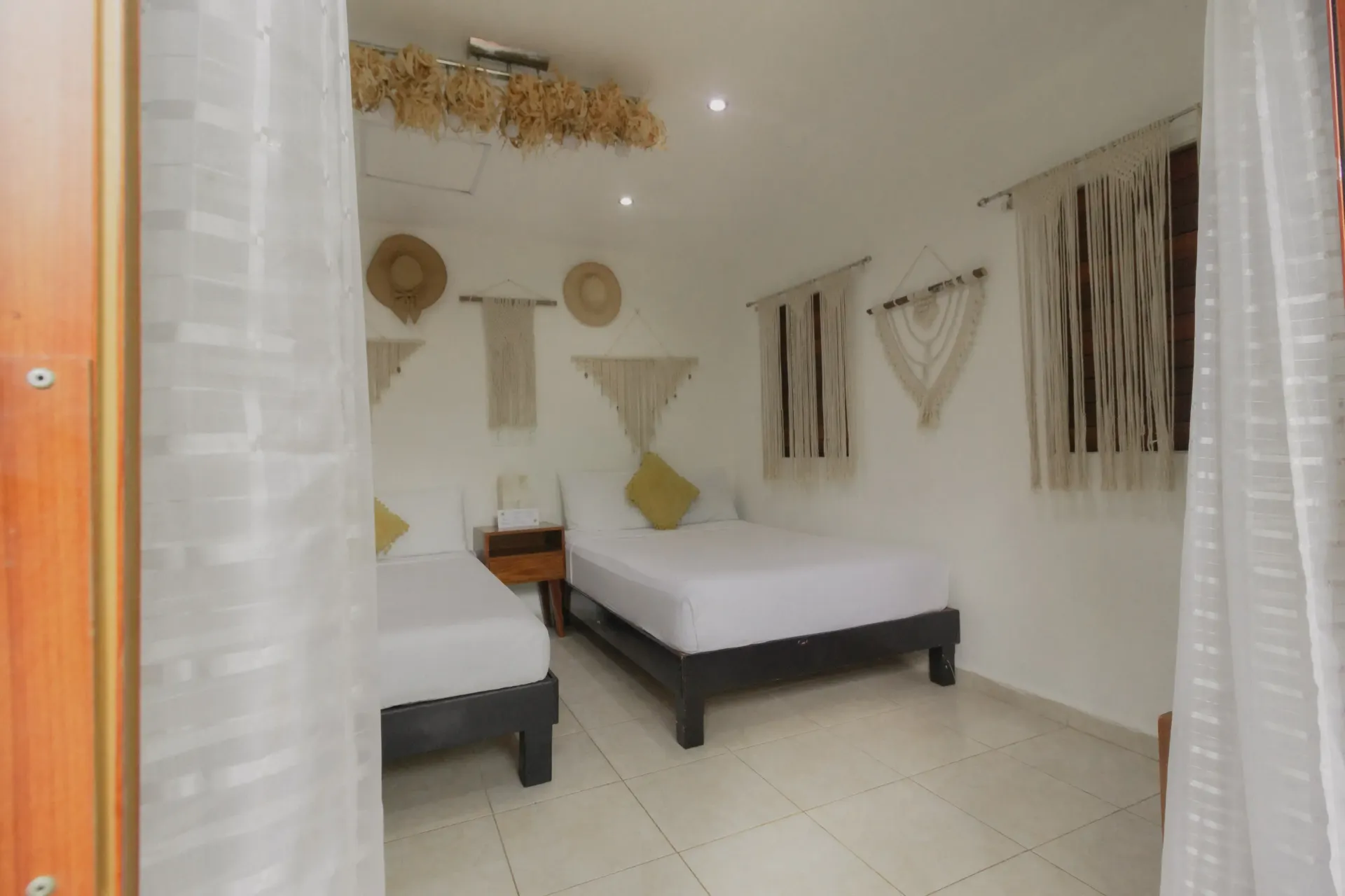 Habitación luminosa y minimalista con dos camas, paredes blancas y decoración de pared tejida.