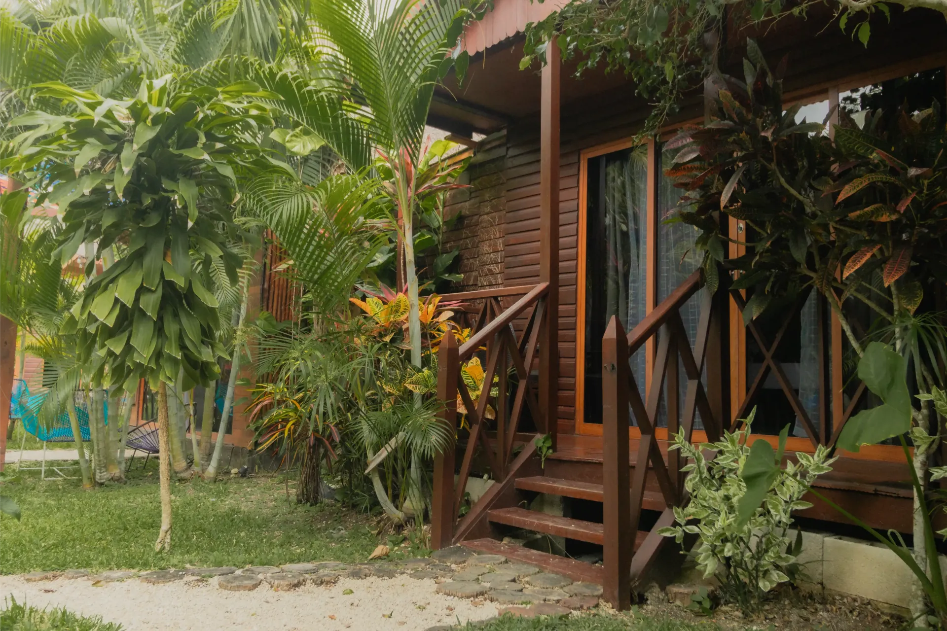 Cabaña tropical de madera con escalones en el porche rodeada de exuberantes plantas y árboles verdes.