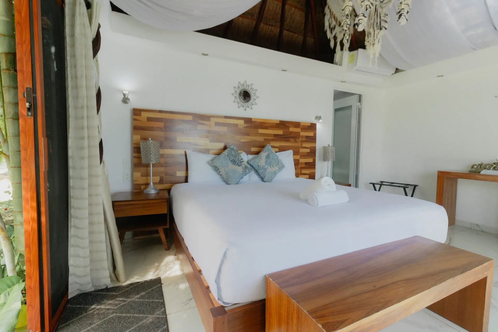Habitación luminosa con cama de madera, sábanas blancas y cabecero decorativo en una habitación rústica.