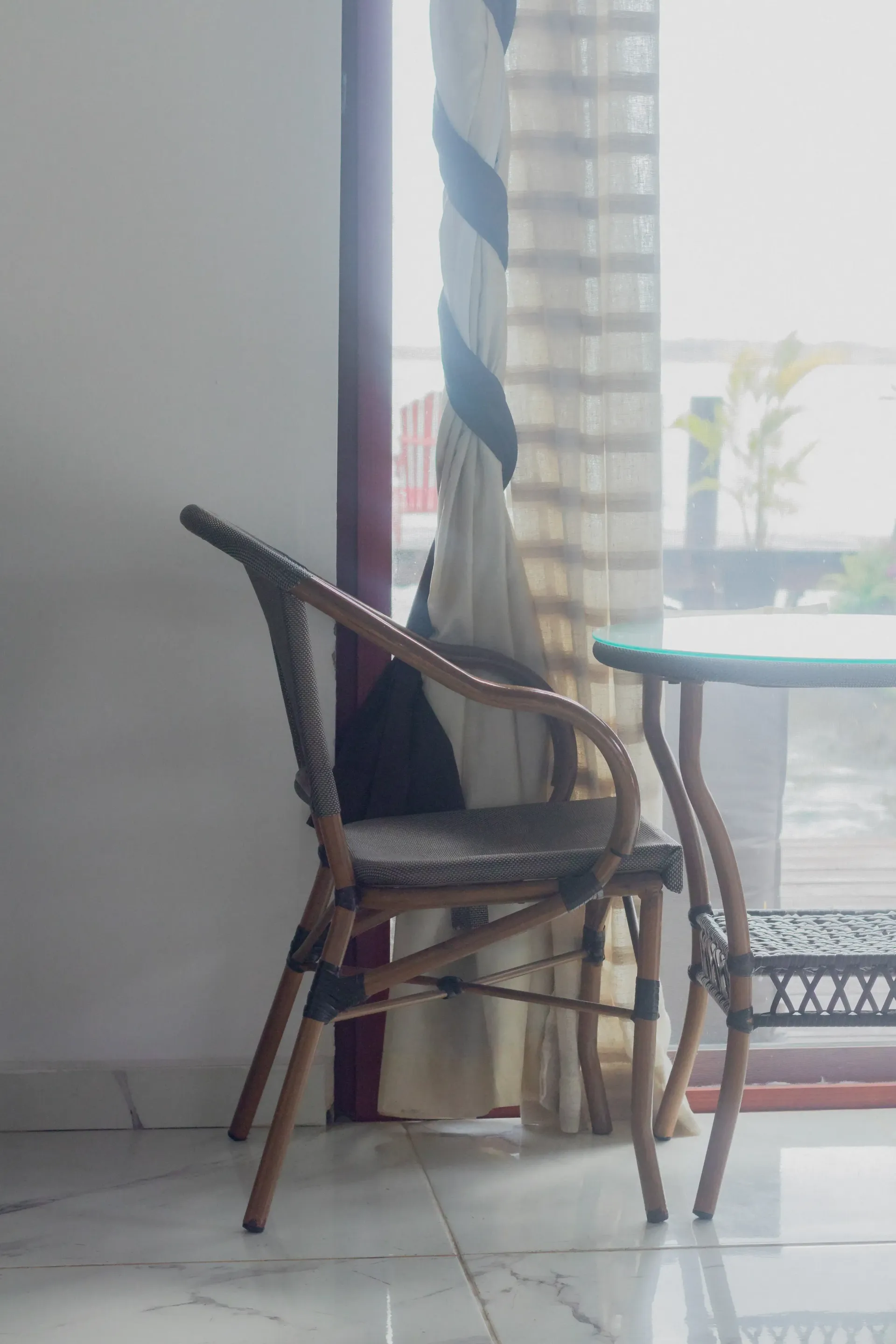 Silla de mimbre junto a una cortina al lado de una ventana en una habitación luminosa.