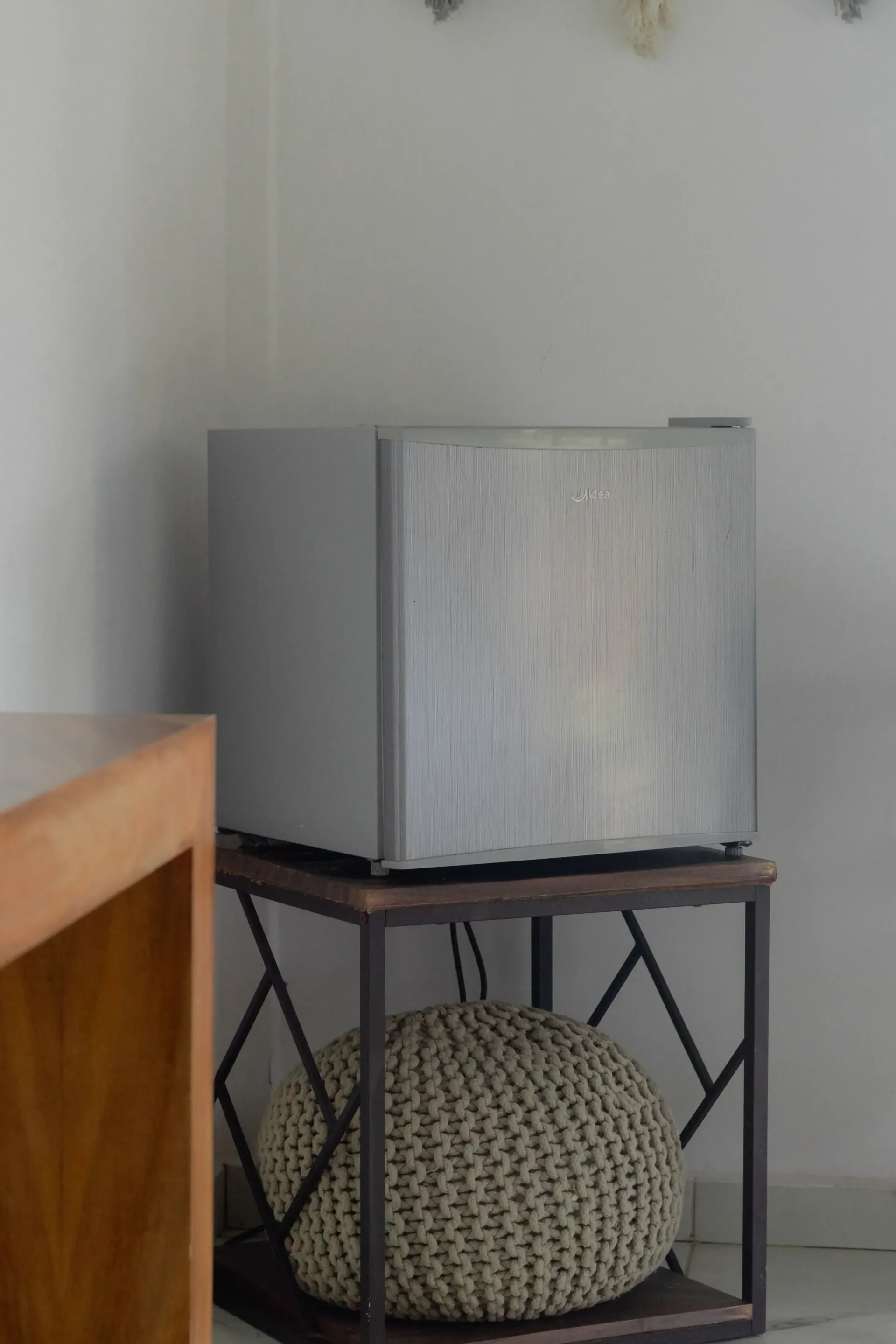 Una caja gris sobre un pequeño soporte de metal con un cojín tejido debajo, junto a una pared en una habitación.