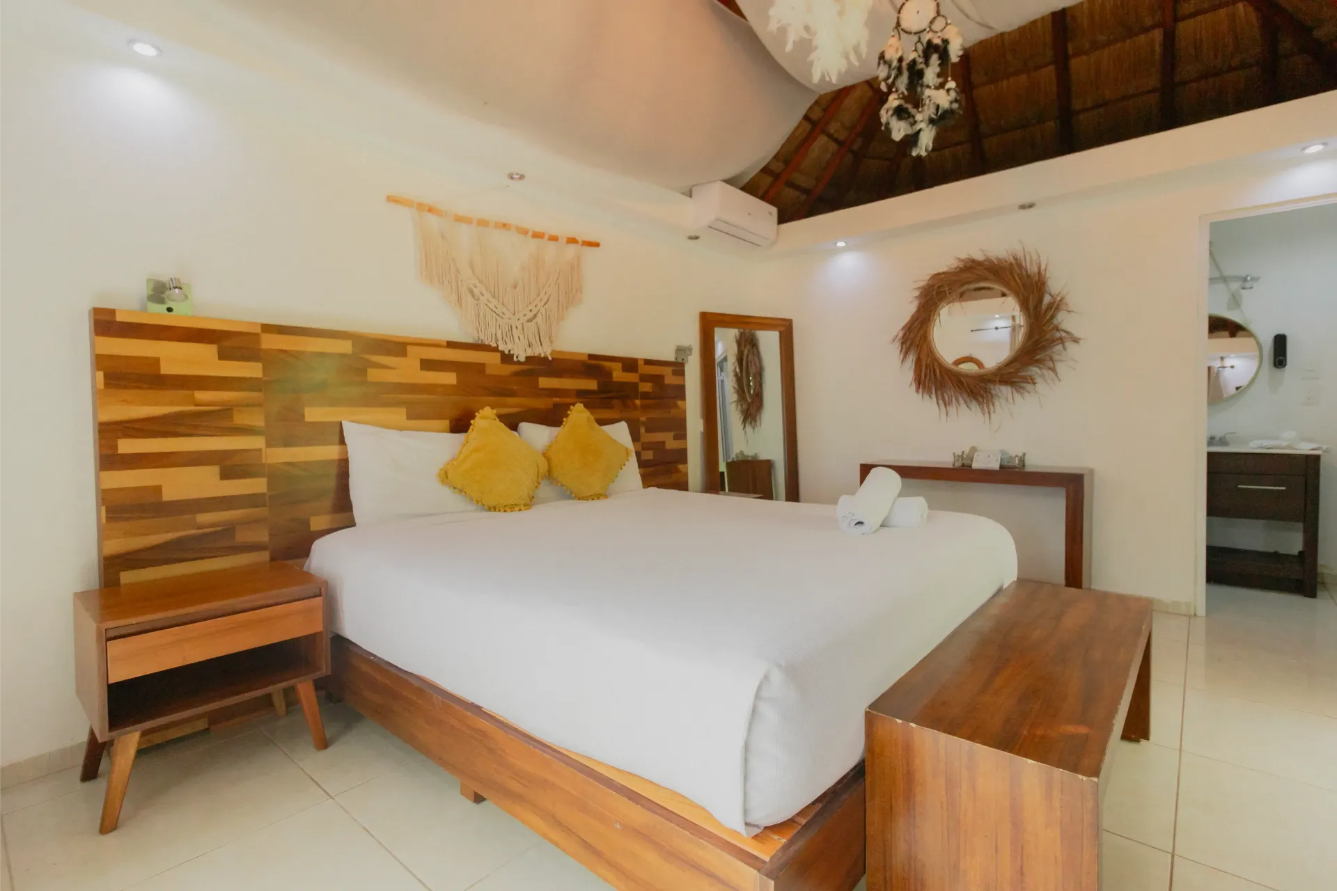 Acogedora habitación con estructura de cama de madera, ropa de cama blanca, almohadas amarillas y decoración rústica.