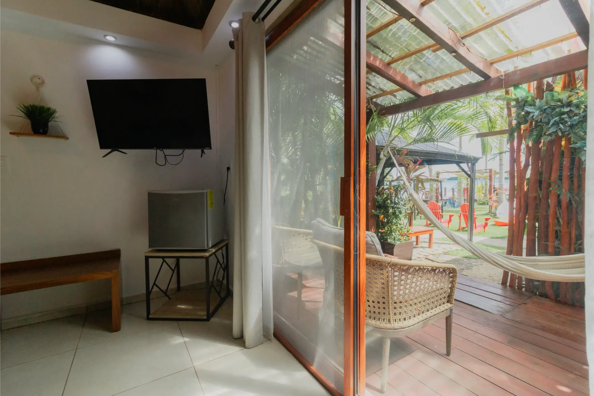 Luminoso salón con acceso a un patio soleado con sillas de mimbre, plantas y una terraza de madera.