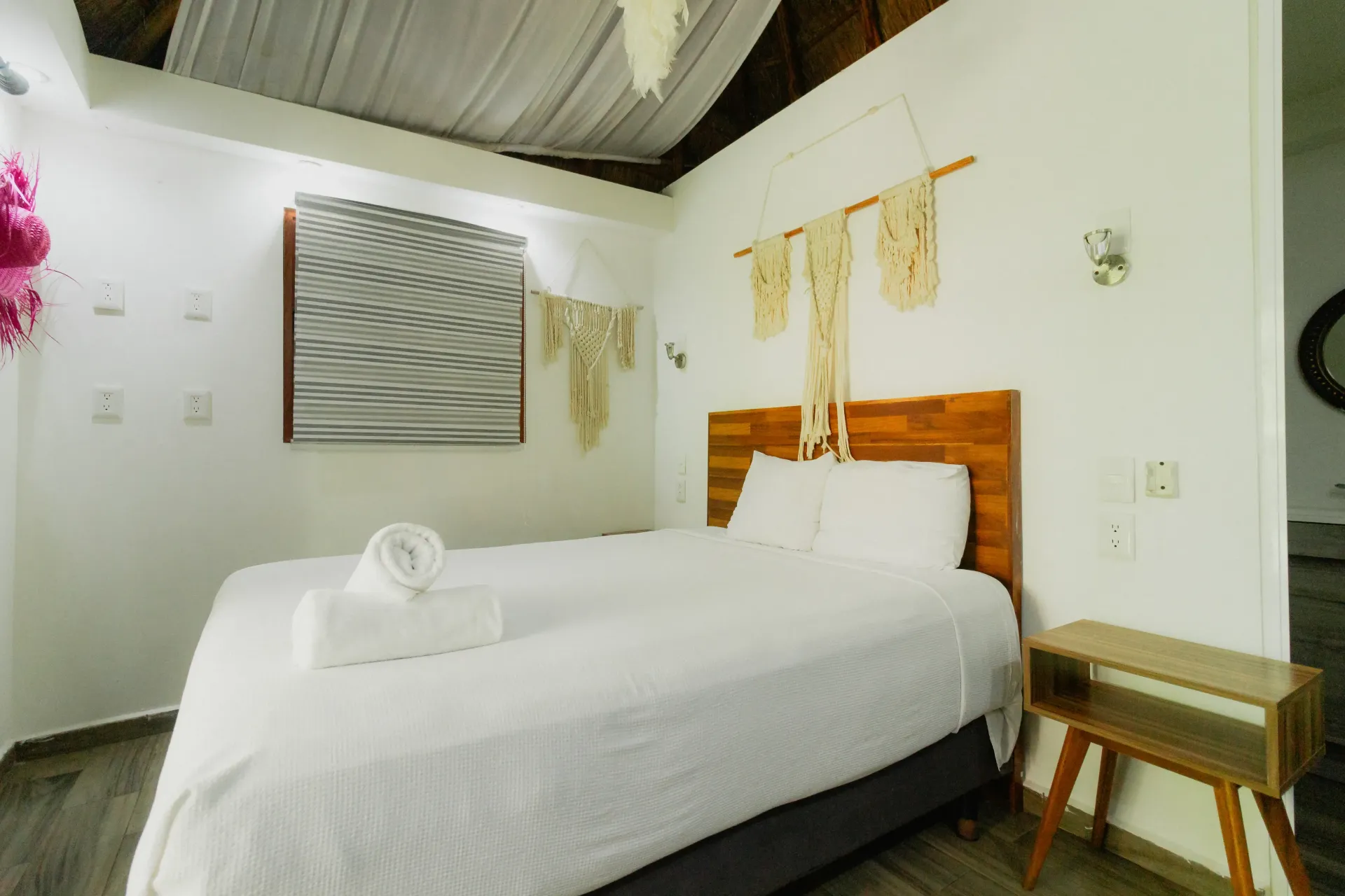 Habitación luminosa con cama blanca, cabecero de madera y decoración de pared suave en un interior sencillo y ordenado.