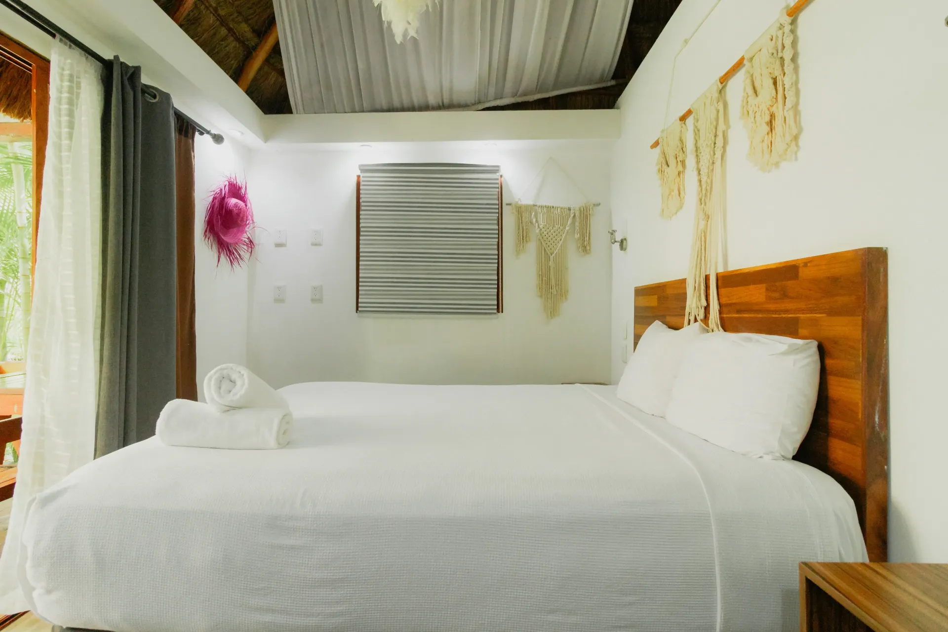 Habitación luminosa con cama blanca, cabecero de madera y cortinas suaves bajo un techo inclinado.