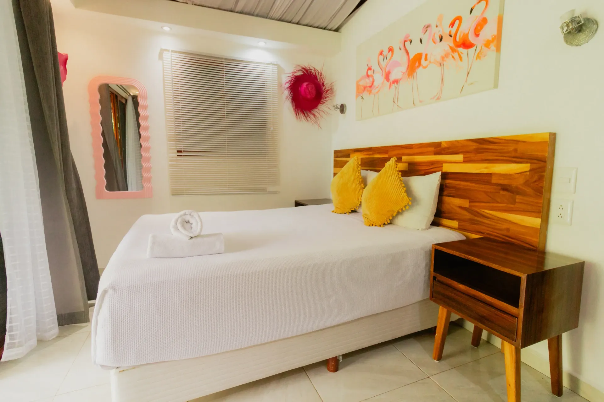 Habitación acogedora con cama blanca, cabecero de madera, almohadas amarillas, cuadros en la pared y una pequeña mesita.