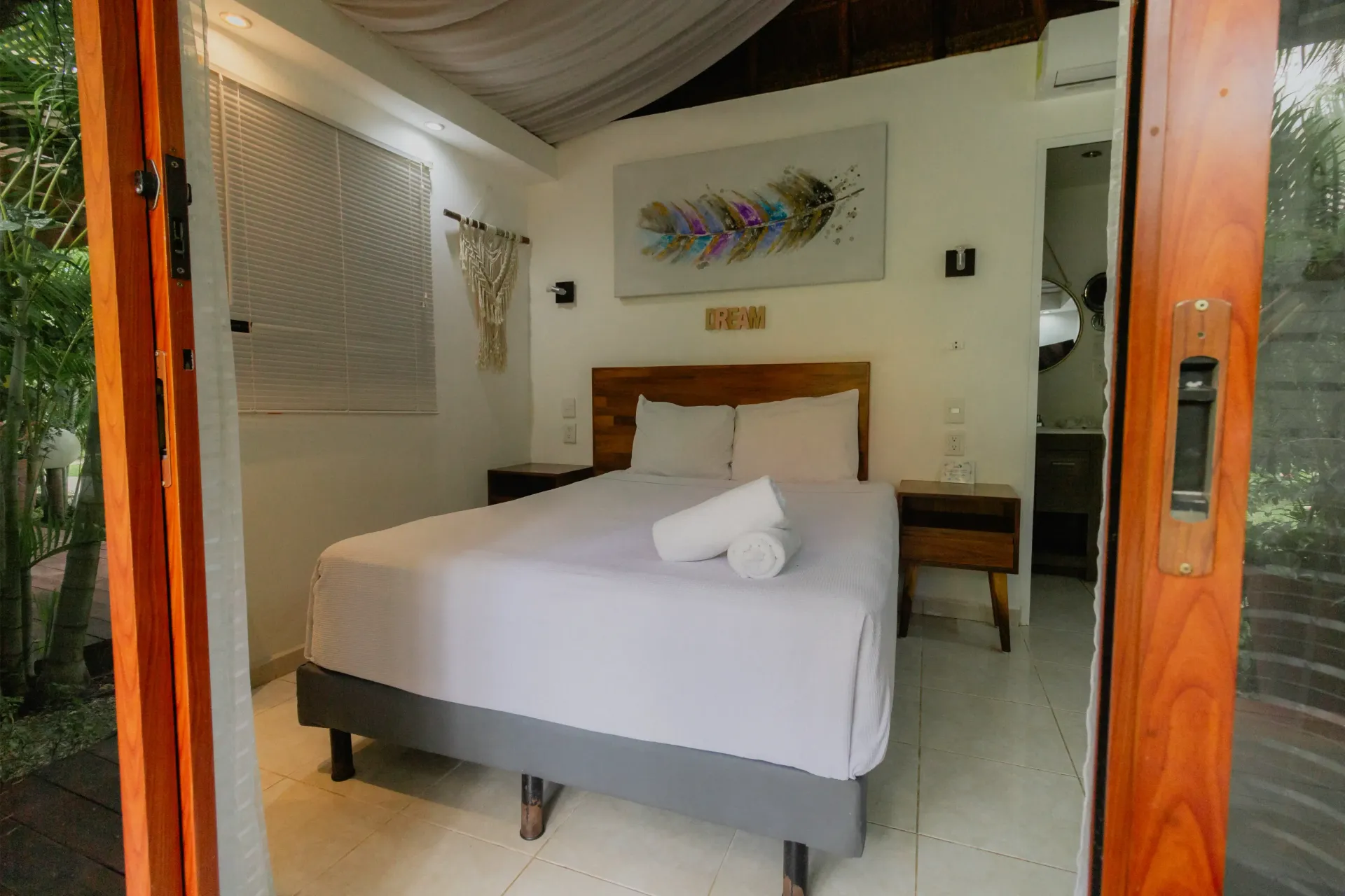 Habitación con dosel blanco, cama bien hecha, cabecero de madera y puertas que dan al exterior.