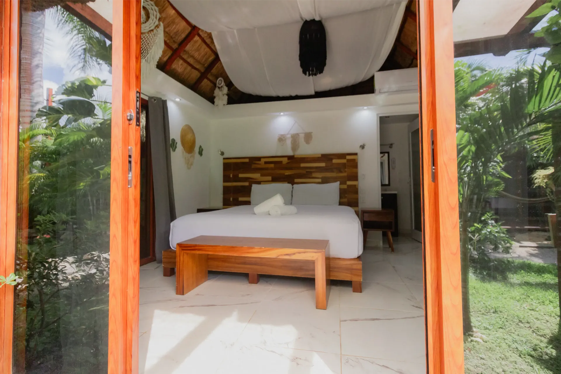 Habitación al aire libre con cama de madera, sábanas blancas y vistas al jardín.