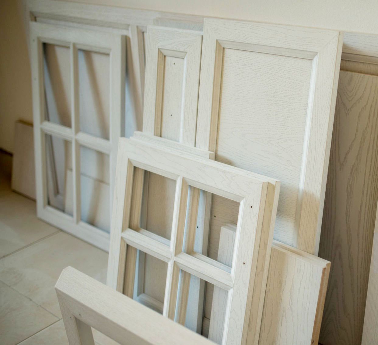 Gli infissi delle finestre e i pannelli delle porte in legno bianco sono appoggiati a una parete.