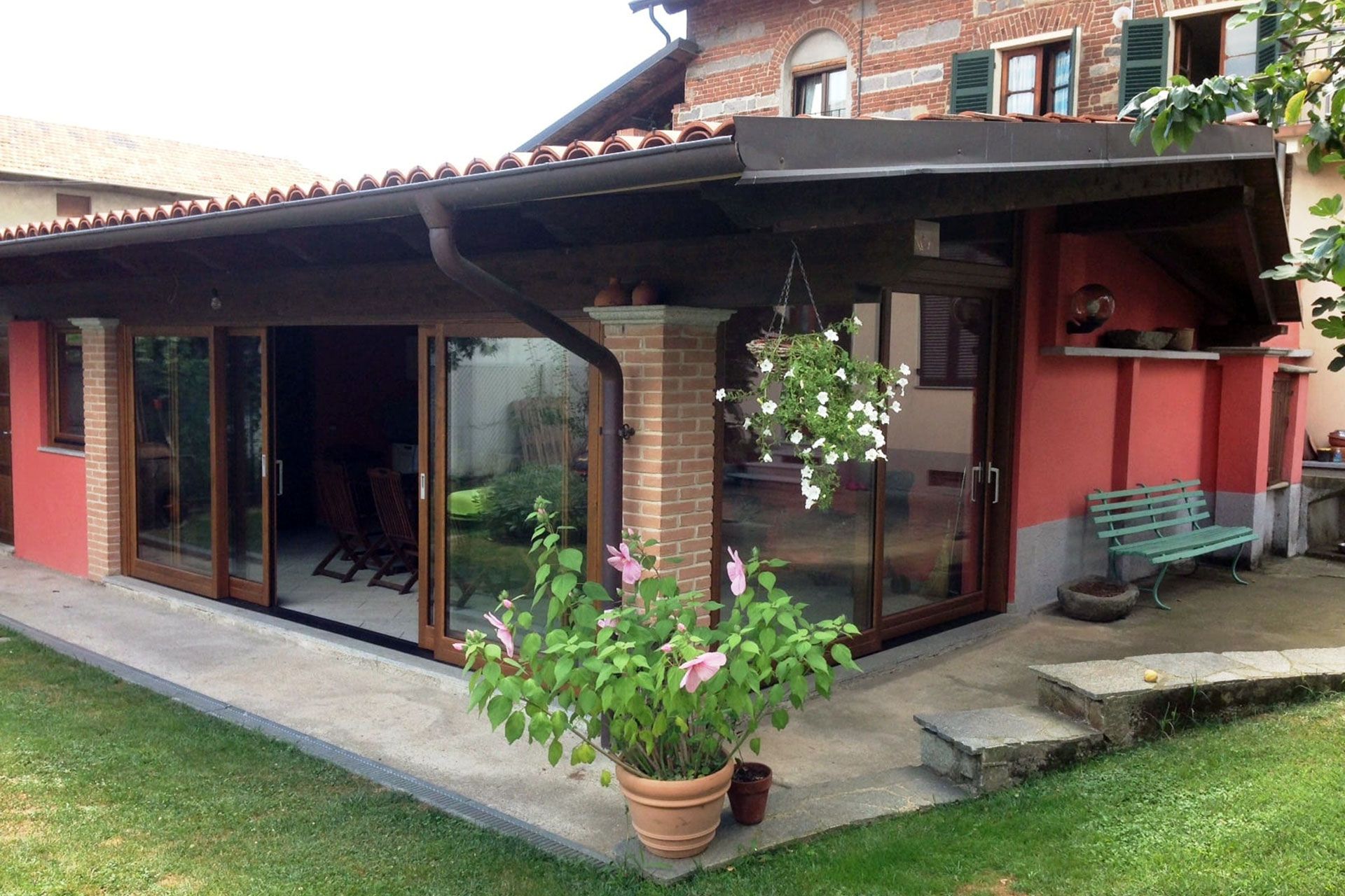 Patio esterno recintato con porte scorrevoli in vetro, pareti rosse e piante in vaso.