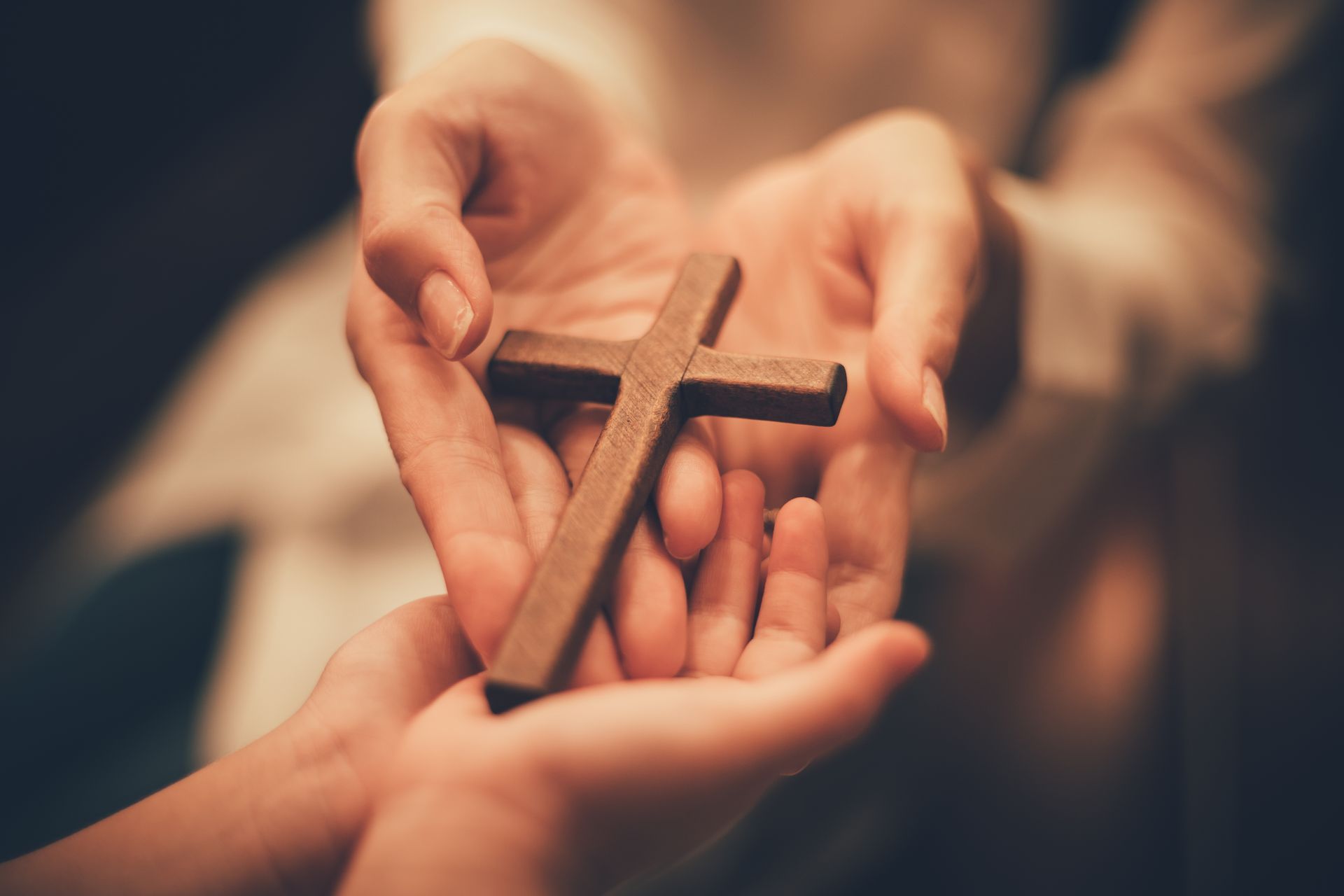 Hands holding out a wooden cross, symbolizing faith and offering.