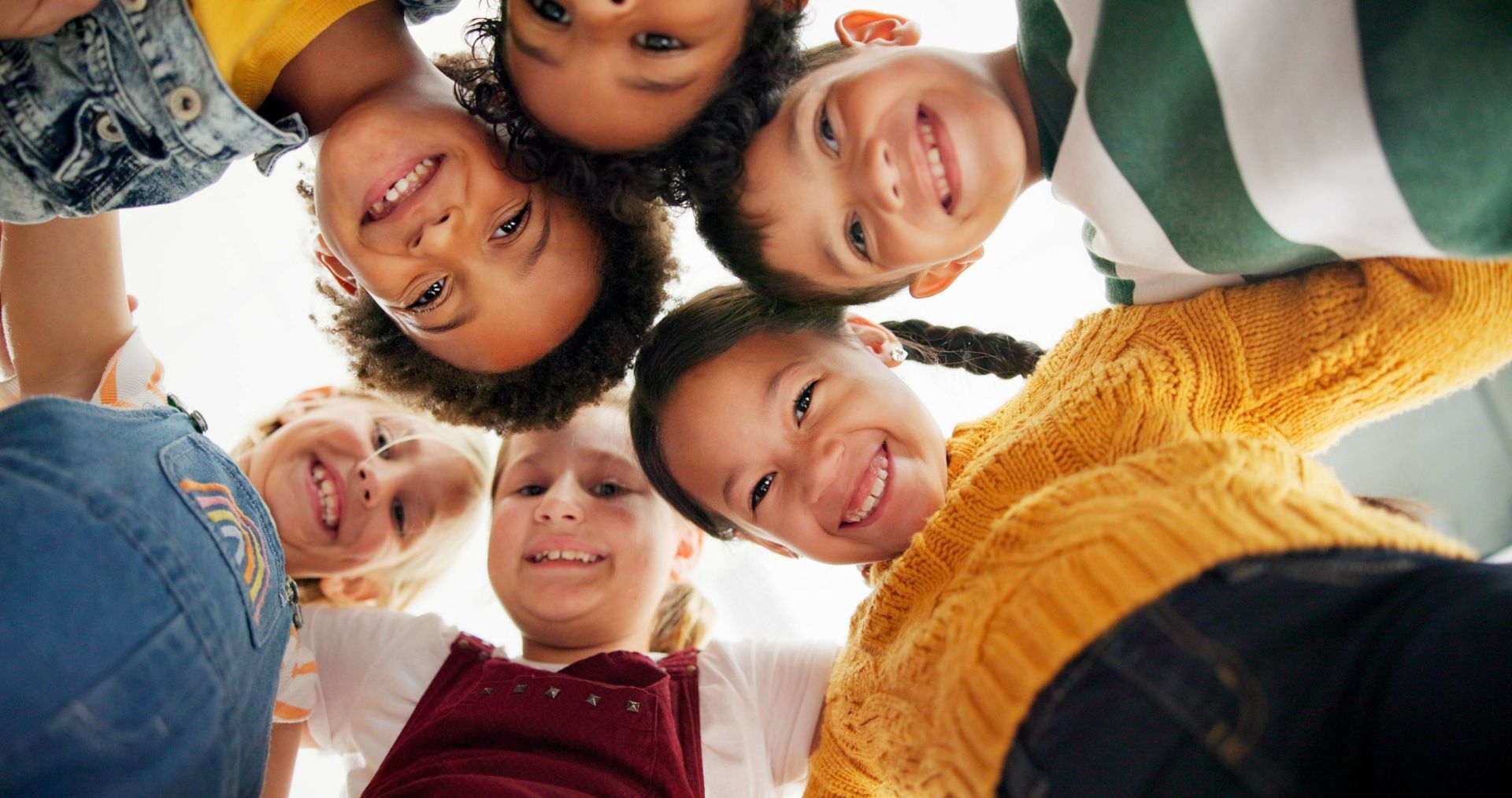 Children smiling, heads together in a circle, looking down.