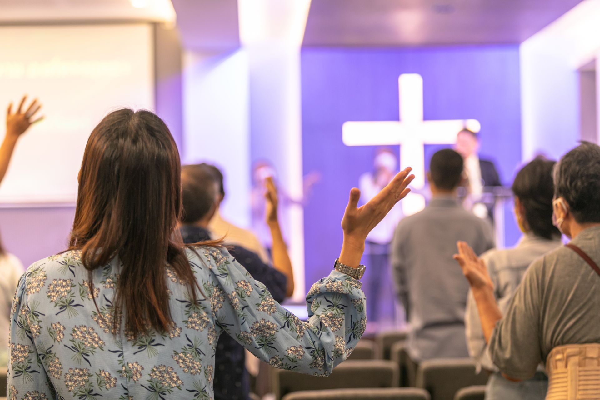 Worship service with people raising hands in a church, a cross on the wall.