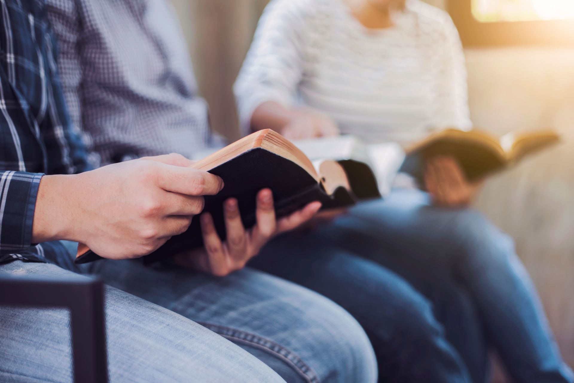 People sitting and reading books together indoors, close-up on hands holding open book.