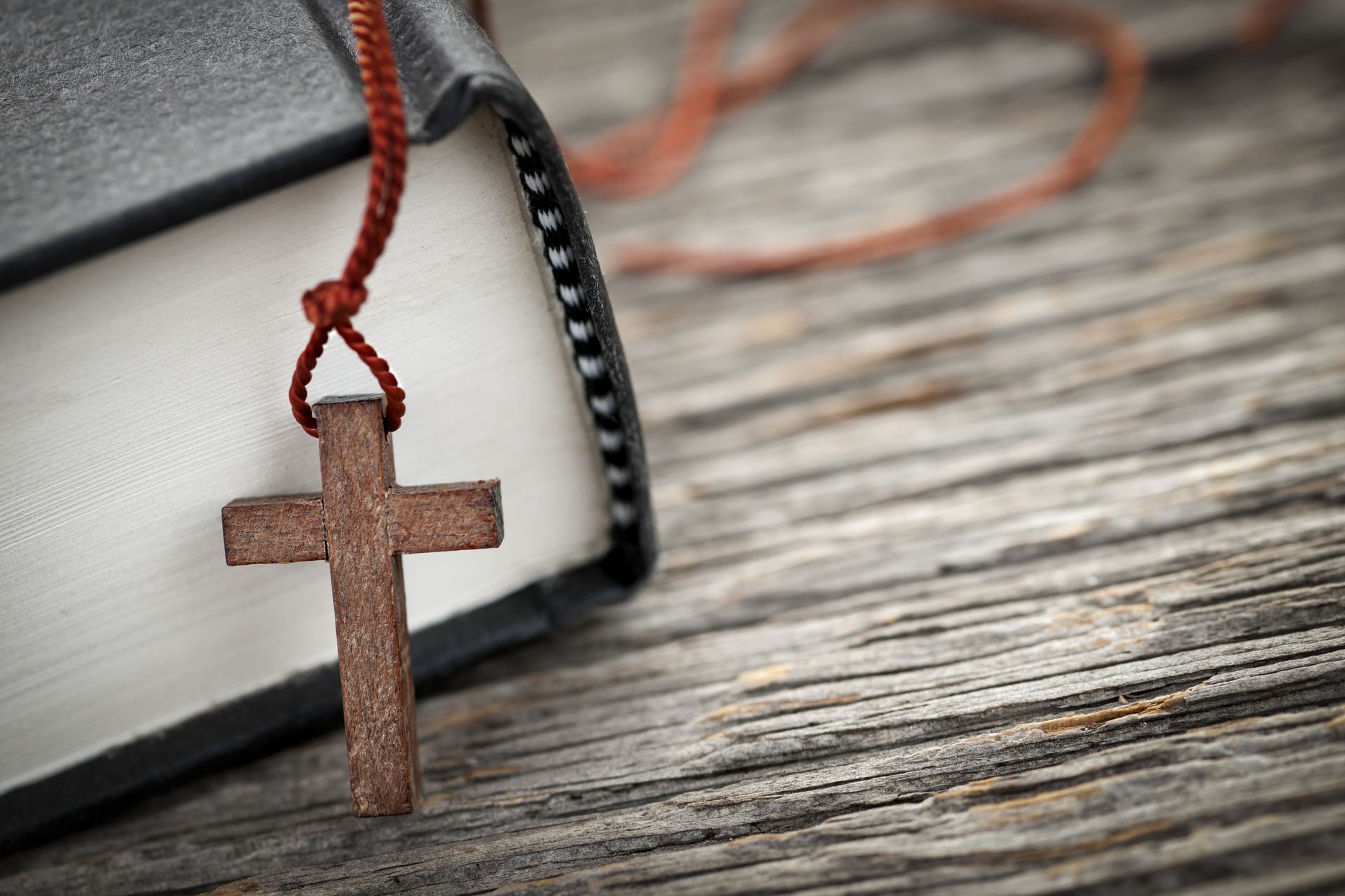 Wooden cross pendant on a closed book, resting on a wood surface.