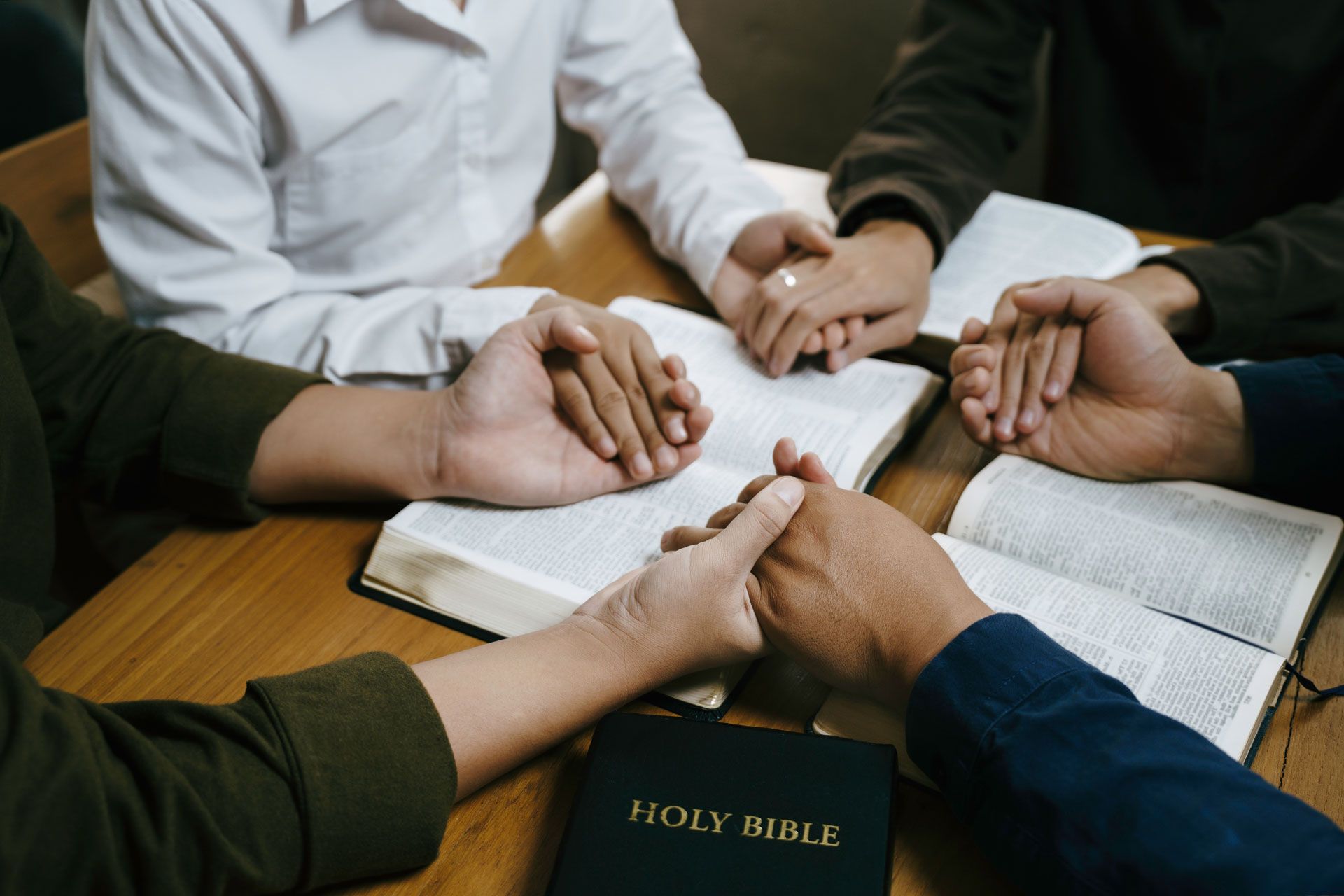 Hands clasped in prayer around open books, likely Bibles, on a table.