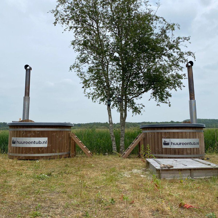 Twee houten hottubs in een veld met een boom op de achtergrond