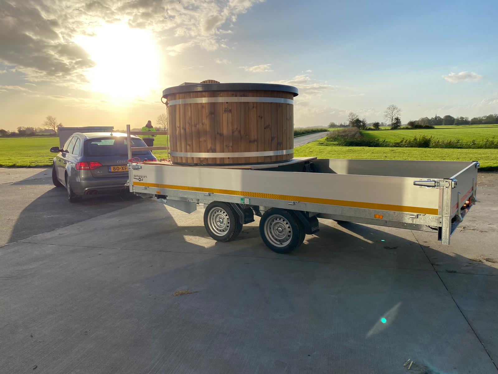 Een auto trekt een houten hottub op een aanhanger.