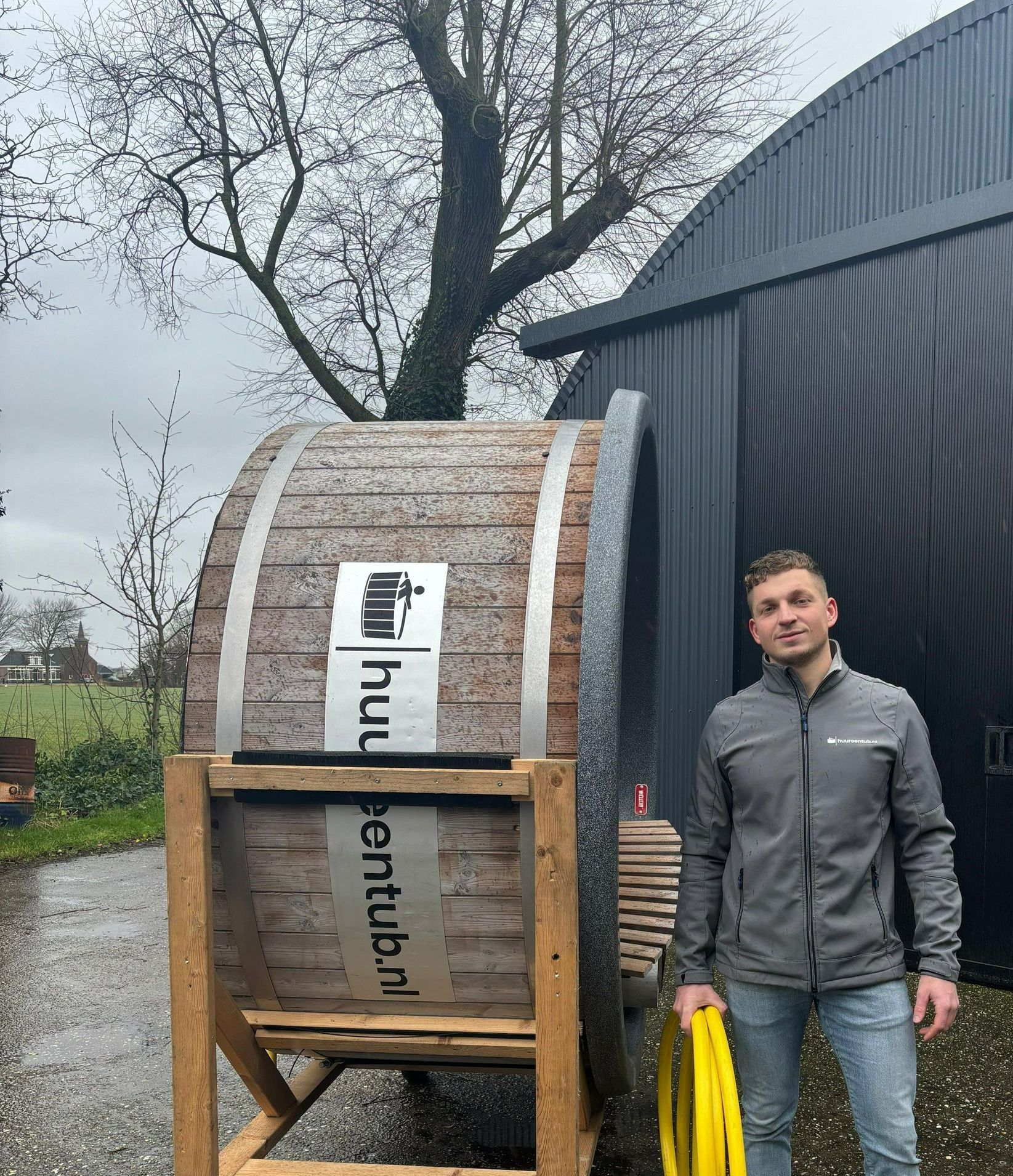 Een man staat voor een houten hottub met logo.