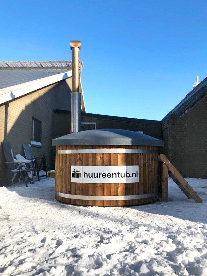 Een houten hottub staat in de sneeuw voor een huis.