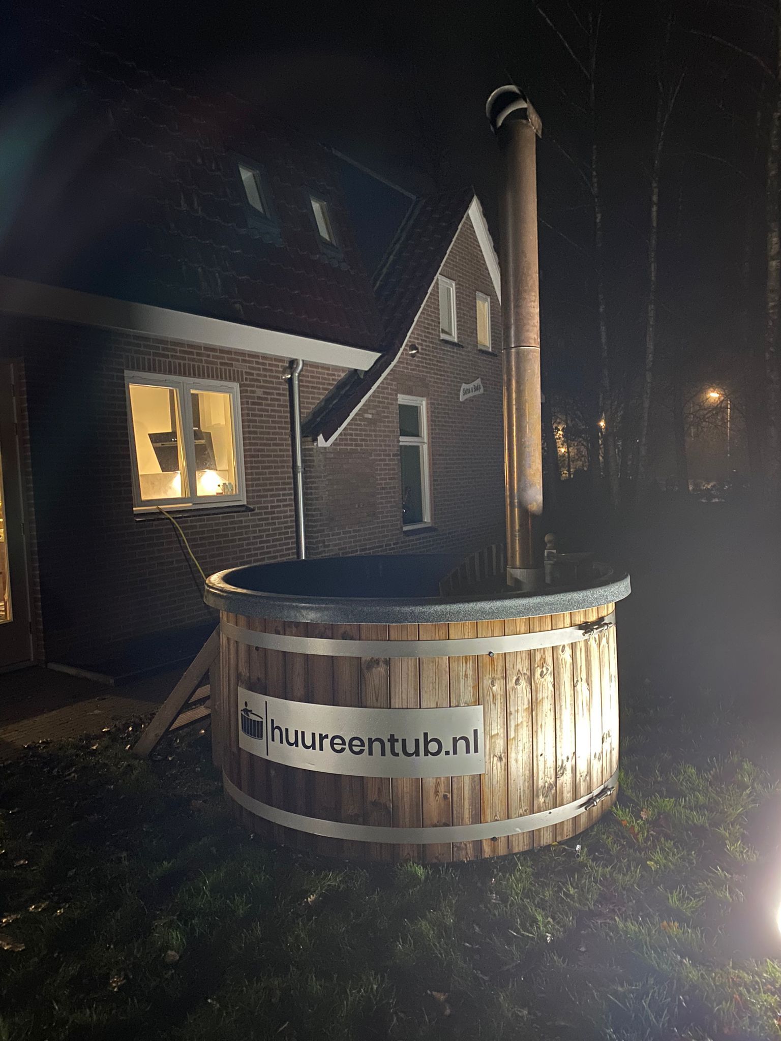 's Nachts staat er een grote houten hottub met logo voor een huis.